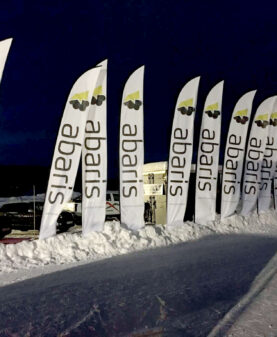 Rekke med profilflagg for Abaris oppstilt i snøen under et kveldsarrangement.