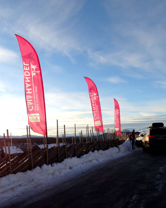 Profileringsflagg montert ved et tradisjonelt tregjerde på en snødekt fjelltopp.