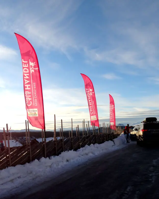 Beachflagg montert ved et tradisjonelt tregjerde på en snødekt fjelltopp.