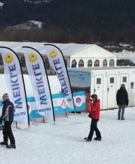 Hvite beachflagg med logo og smilefjes plassert foran et stort arrangementstelt i fjellet.