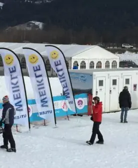 Hvite beachflagg med logo og smilefjes plassert foran et stort arrangementstelt i fjellet.