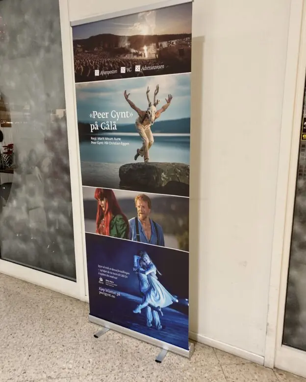 En rollup-banner står på gulvet og viser reklame for Peer Gynt på Gålå med flere bilder fra forestillingen.