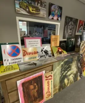 Flere skilt og reklameprodukter, som et parkeringsforbudt-skilt og Diplom-Is-reklamer, ofte laget med klistremerker, utstilt.