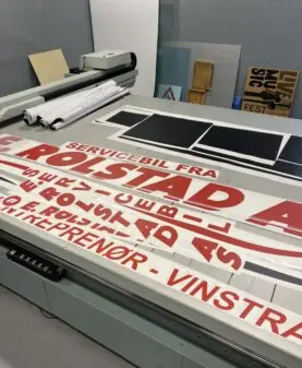 Røde og hvite klistremerker med tekst for bildekor ligger utover en stor arbeidsbenk.