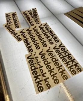 Brune klistremerker med svart Veidekke-logo ligger på et opplyst bord.