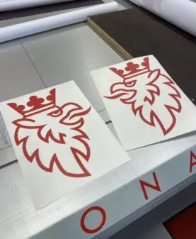 To røde klistremerker med Scania-logoen, en kronet griff, ligger på en arbeidsbenk.