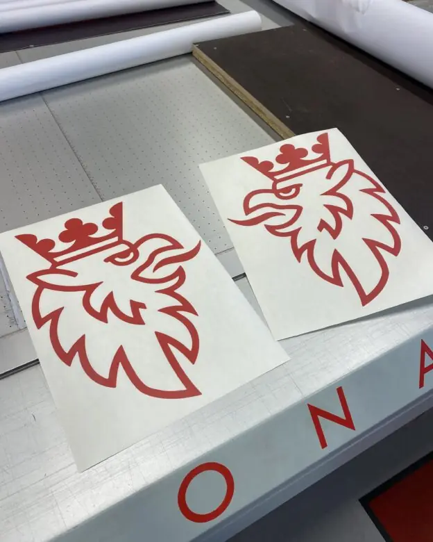 To røde klistremerker med Scania-logoen, en kronet griff, ligger på en arbeidsbenk.