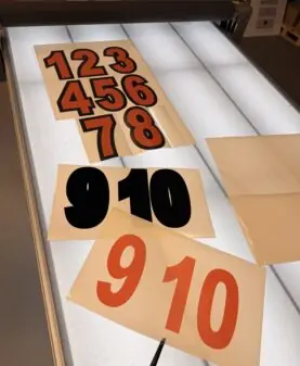 Utskårne klistremerker med tallene 1-10 i ulike farger ligger på et opplyst arbeidsbord.