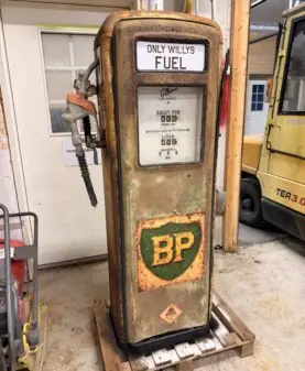 En rusten, gammel bensinpumpe med en BP-logo som ser ut som et klistremerke, står på en trepall.