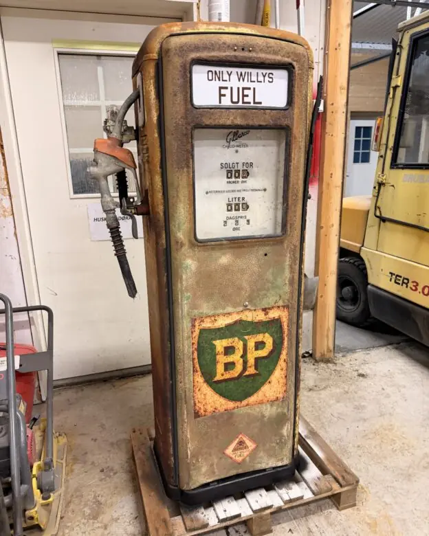 En rusten, gammel bensinpumpe med en BP-logo som ser ut som et klistremerke, står på en trepall.