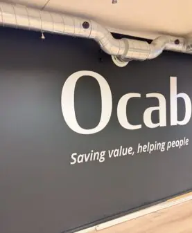 Store hvite klistremerker med Ocab-logo og slagord på en mørkegrå vegg.