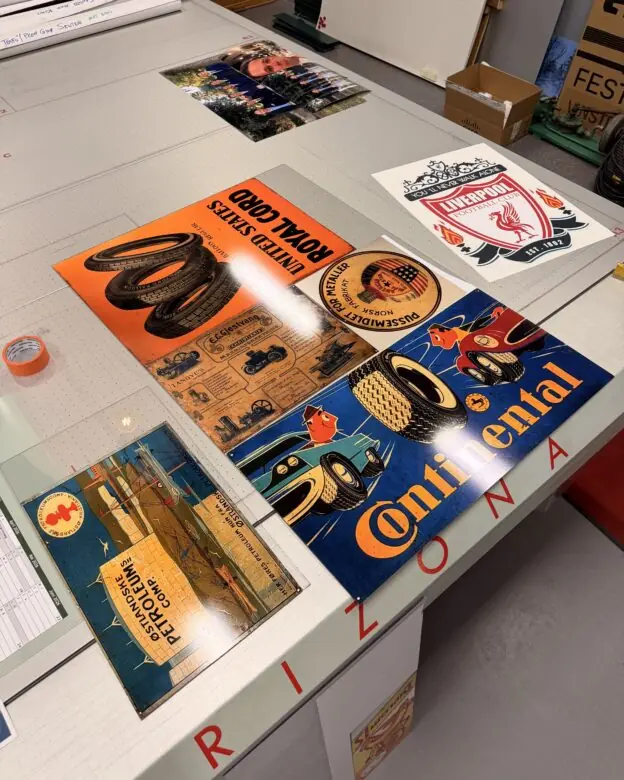 Flere retro klistremerker med vintage reklame for dekk og en Liverpool FC-logo ligger spredt på et lyst bord.