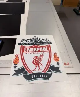 Et stort klistremerke med Liverpool Football Clubs logo ligger på et arbeidsbord.