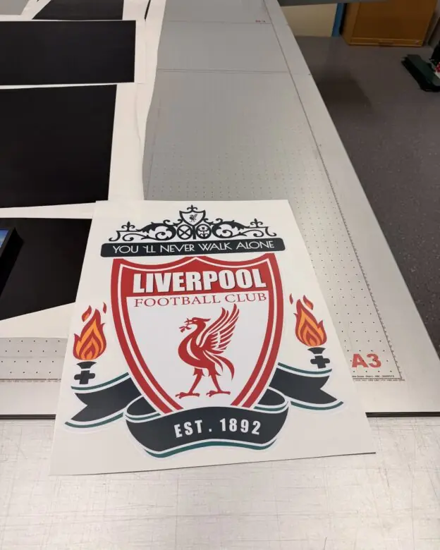 Et stort klistremerke med Liverpool Football Clubs logo ligger på et arbeidsbord.