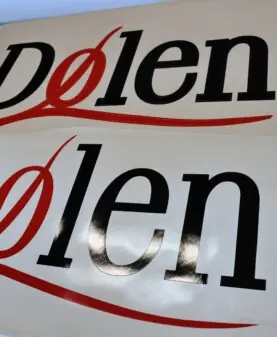 To hvite ark med Dølen-logoer, som er klistremerker, ligger side om side.