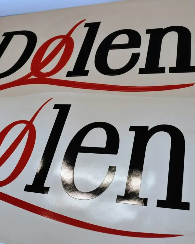 To hvite ark med Dølen-logoer, som er klistremerker, ligger side om side.