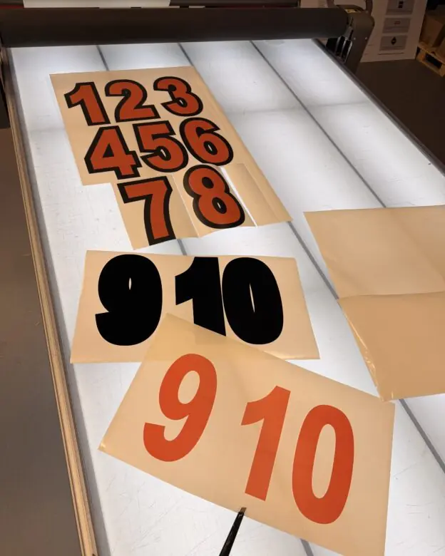Utskårne klistremerker med tallene 1-10 i ulike farger ligger på et opplyst arbeidsbord.