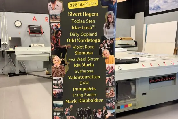 En svart rollup-banner for Rondaståkk festival med artistnavn og små bilder står i et trykkeri.