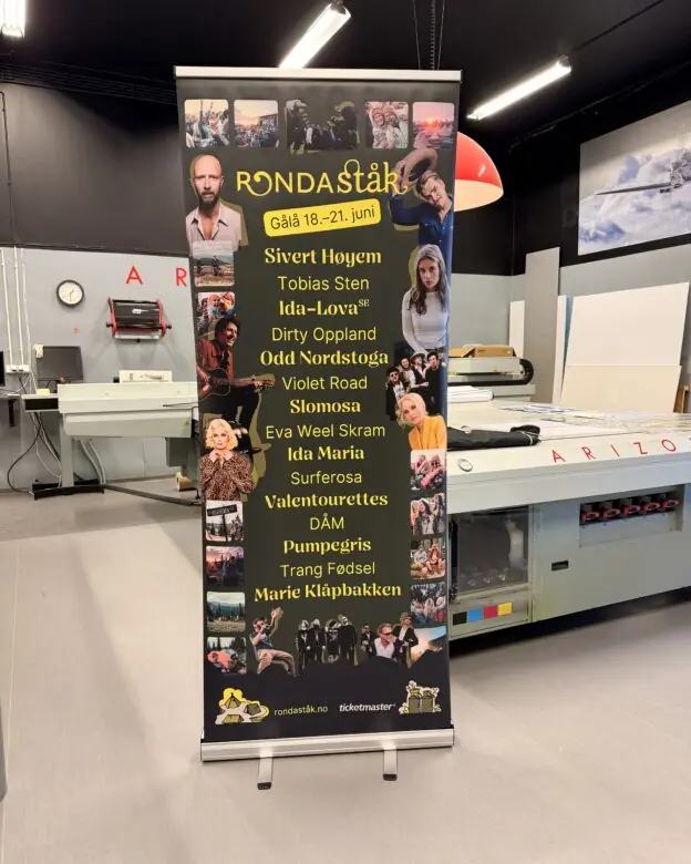 En svart rollup-banner for Rondaståkk festival med artistnavn og små bilder står i et trykkeri.